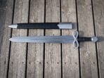 Damascus sword with infinity loop guard and round engraved pommel lying below its black scabbard on wooden decking
