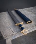 Damascus Viking sword with brass hilt and blue leather scabbard with brass throat laid on a weathered table