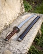 Damascus wakizashi with brown leather wrapped handle and knotwork engraved round guard beside its dark wooden saya