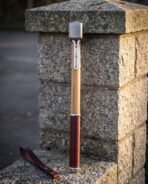 Damascus war hammer seen edge on standing against a granite pillar with ash haft, steel langets and leather grip