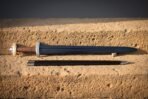 Dark blued Viking sword with brown leather grip and lobed pommel lying above its black scabbard on sandstone