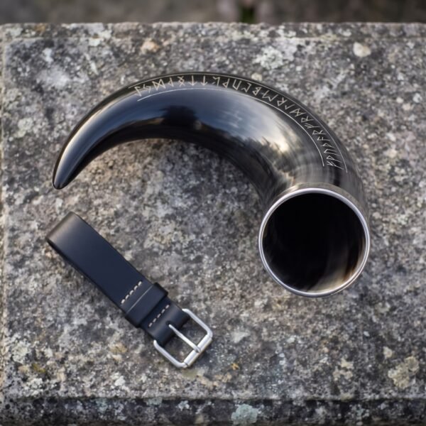 Dark natural ox horn drinking horn with carved rune row and steel rim beside a black leather belt loop on granite