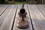 Dark ox horn drinking horn seen from the mouth end, sitting in its turned walnut stand with a knotwork carved base on decking