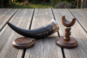 Dark ox horn drinking horn with stand in turned walnut, steel rim band and a carved knotwork coaster, photographed on weathered decking in low sun