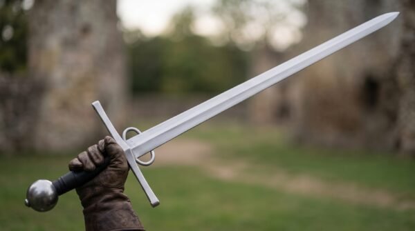 Gloved hand raising a side ring arming sword trainer with black grip and sphere pommel on a castle lawn