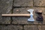 Double bit axe with light ash haft laid flat on stone paving next to its buckled brown leather head cover