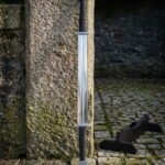 Double ended viking sword with a Celtic knotwork pommel at each end and twin cord wrapped grips standing against a granite pillar on mossy cobblestones