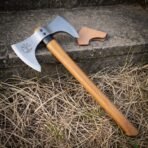 Double headed axe with bearded front bit and hooked rear bit lying across dry grass on a stone step beside its leather cover