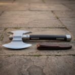 Double headed axe with dark haft and steel inlays lying on flagstones beside its brown leather edge sheath