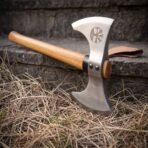 Double headed axe with Vegvisir and tree etching on the polished head and oak haft resting on a stone step in dry grass