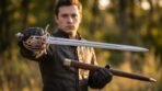 High carbon steel broadsword with pierced shell guard and red panels held out by a young man gripping its brown scabbard