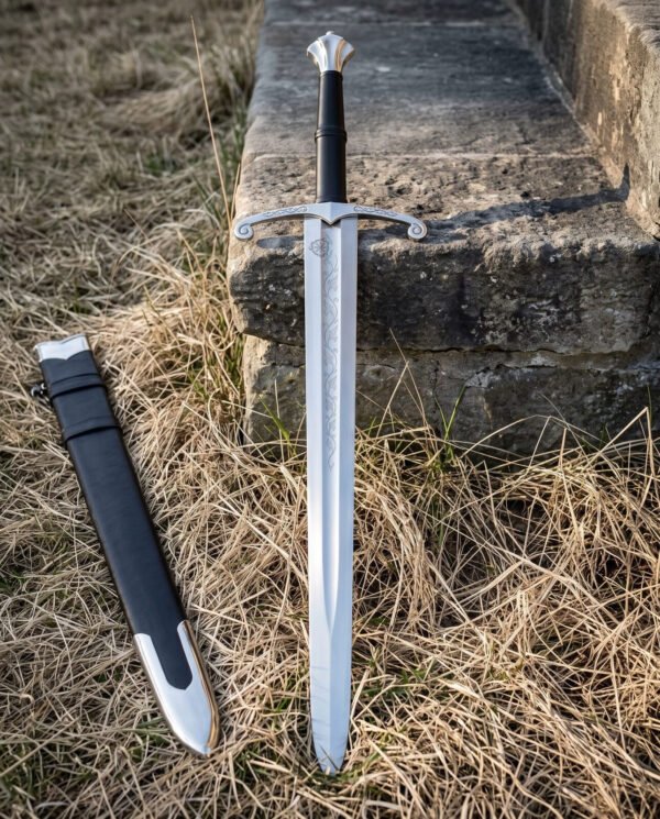 Elven sword standing point down in dry grass before an old stone step, fluted crown pommel and scrolled guard above a blade etched with flowing vine scrollwork