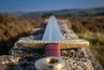 Engraved brass crossguard and brass ring pommel of a steel Viking sword with red leather grip on a dry stone wall
