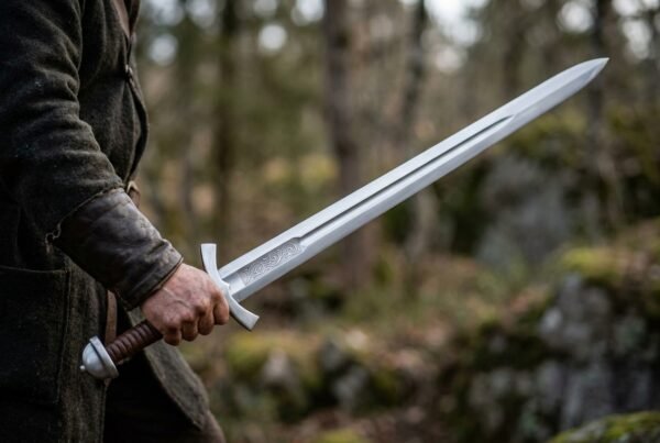 Engraved high carbon steel Viking sword with downswept cross held out in one hand in a rocky forest