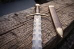 Engraved knotwork panel cut into the brass guard, dark brown leather grip below it