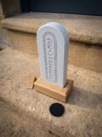 Engraved slate rune stone with rounded top in an oak display base seen from the side on a sandstone step, felt pad in front