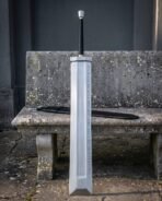 Fantasy greatsword with slab sided steel blade and rune lines standing upright against a stone bench with its black scabbard