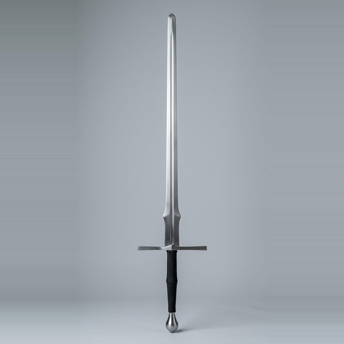 Feder sword with a flat ricasso and schilt lobe Feder sword with a flat parallel ricasso, a discrete schilt lobe, narrow blade to a broad rolled tip and a black cord wrapped two handed grip shown against a plain studio backdrop