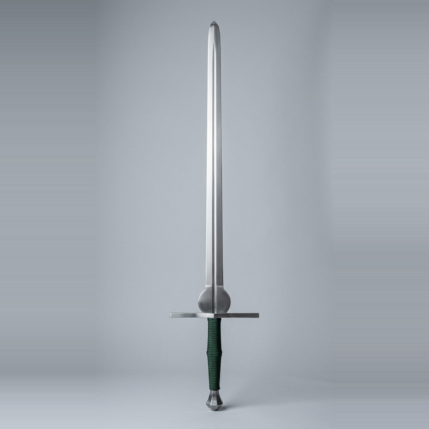 Vindlaur feder training sword RK-3007 Feder training sword with a rounded schilt above the ricasso, scent stopper pommel and dark green cord wrapped two hand grip standing against a plain studio backdrop