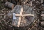 Felling axe with knotwork panel and curved haft lying on a split log over a stump, brown leather blade mask beside it, overhead view