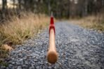 Felling axe with red enamelled head and polished bevel on a long hickory handle viewed end on along a gravel path