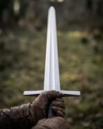 First person view of a high carbon steel arming sword held upright in gloved hands, cross guard and fuller in focus