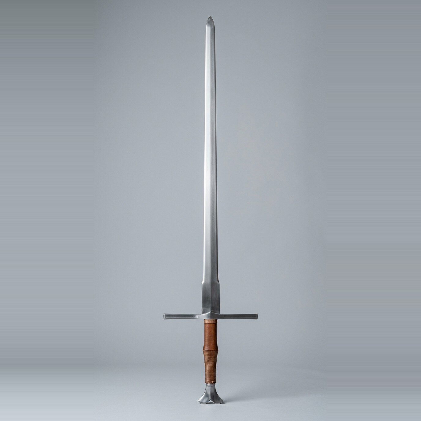Valkspire Ricasso Longsword RK-3012 Fishtail pommel longsword with a squared wide ricasso, tan leather and cord grip standing point up against a plain grey studio backdrop