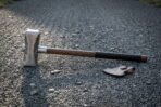Forged viking war hammer with a hammer textured steel head, a runic inscription and a leather wrapped hardwood haft, lying on a gravel track in low evening light