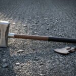 Forged viking war hammer with a hammer textured steel head, a runic inscription and a leather wrapped hardwood haft, lying on a gravel track in low evening light