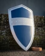 Front view of a blue steel heater shield with riveted polished border and Celtic knotwork band against a mossy wall