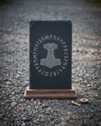 Front view of a slate rune plaque with knotwork Mjolnir on a dark walnut base, brass fixing screw lying beside it