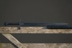 Full length blackened sword with Valknut mark on the blade laid on a grey fence rail above its black scabbard