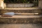 Full length Viking spear with steel leaf head, pale ash haft and brass butt cap laid along a sandstone step
