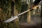 Glaive polearm with a hooked steel head and pale ash haft held in gloved hands on a misty woodland path