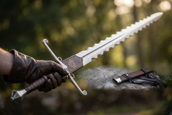 Gloved hand gripping a wavy edged arming sword with scrolled guard and Valknut leather rain guard in a sunny forest