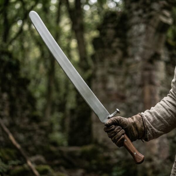 Gloved hand holding a steel dussack trainer with rounded tip, steel nagel and wooden grip in front of forest ruins