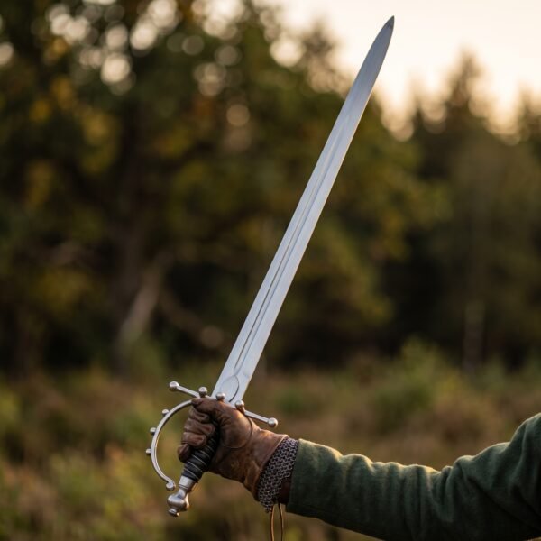 Gloved hand holding up a steel spadroon trainer with five ball knuckle bow guard and wire bound grip in a forest