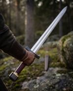 Gloved hand holding a Viking arming sword with blackened guard and pommel aloft in a pine forest