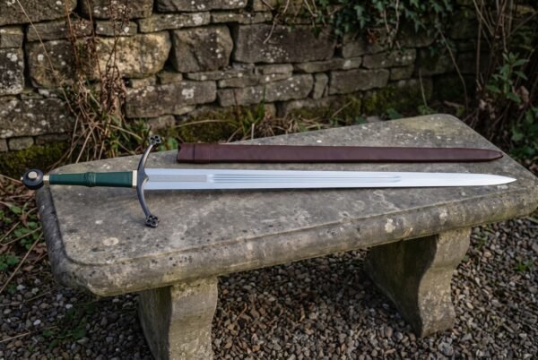 Green leather arming sword displayed on a stone bench with its brown scabbard, showing the blackened quatrefoil crossguard, triple fullered polished blade and etched knotwork band.