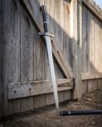 Hand and a half longsword with navy leather grip and faceted pommel leaning on a weathered wooden fence