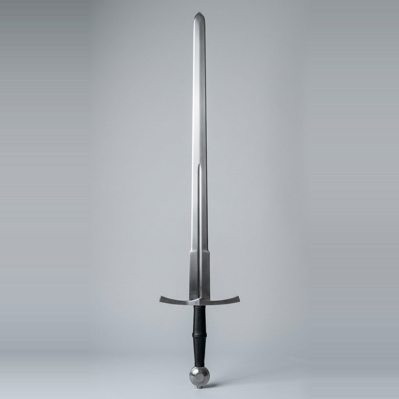 Vardholt Hand and a Half Blunt Longsword RK-3008 Hand and a half trainer with a narrow fuller, wheel pommel and black waisted leather grip standing point up against a plain grey studio backdrop