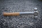 Hand forged 1095 steel blacksmith hammer with mirror polished ball pein head, Elder Futhark runes on the shank and an ash grip resting on grey gravel