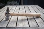 Hand forged 1095 steel cross pein hammer with a mirror polished head, engraved knotwork cheek and shaped hickory handle lying on a weathered wooden table