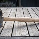 Hand forged 1095 steel cross pein hammer with a mirror polished head, engraved knotwork cheek and shaped hickory handle lying on a weathered wooden table