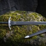 Hand forged 1095 steel sawback fantasy sword with a spiked crossguard and black scabbard lying on a moss covered boulder in shadowed woodland