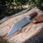 Hand forged 1095 steel Viking seax knife with etched raven, angled close view of the blade on a weathered forest log