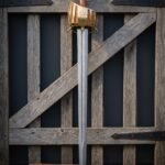 Hand forged brass basket hilt sword against an old wooden gate, damascus blade below a Vegvisir engraved brass cage, tan leather grip and matching leather scabbard