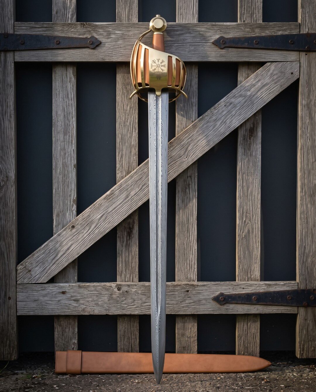 Hand forged brass basket hilt sword against an old wooden gate, damascus blade below a Vegvisir engraved brass cage, tan Hand forged brass basket hilt sword against an old wooden gate, damascus blade below a Vegvisir engraved brass cage, tan leather grip and matching leather scabbard