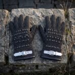 Hand forged chainmail and leather gauntlets with buckled cuffs laid side by side on a flat stone wall, seen from above