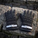 Hand forged chainmail and leather gauntlets with domed steel studs and buckled cuffs, angled close view on weathered stone